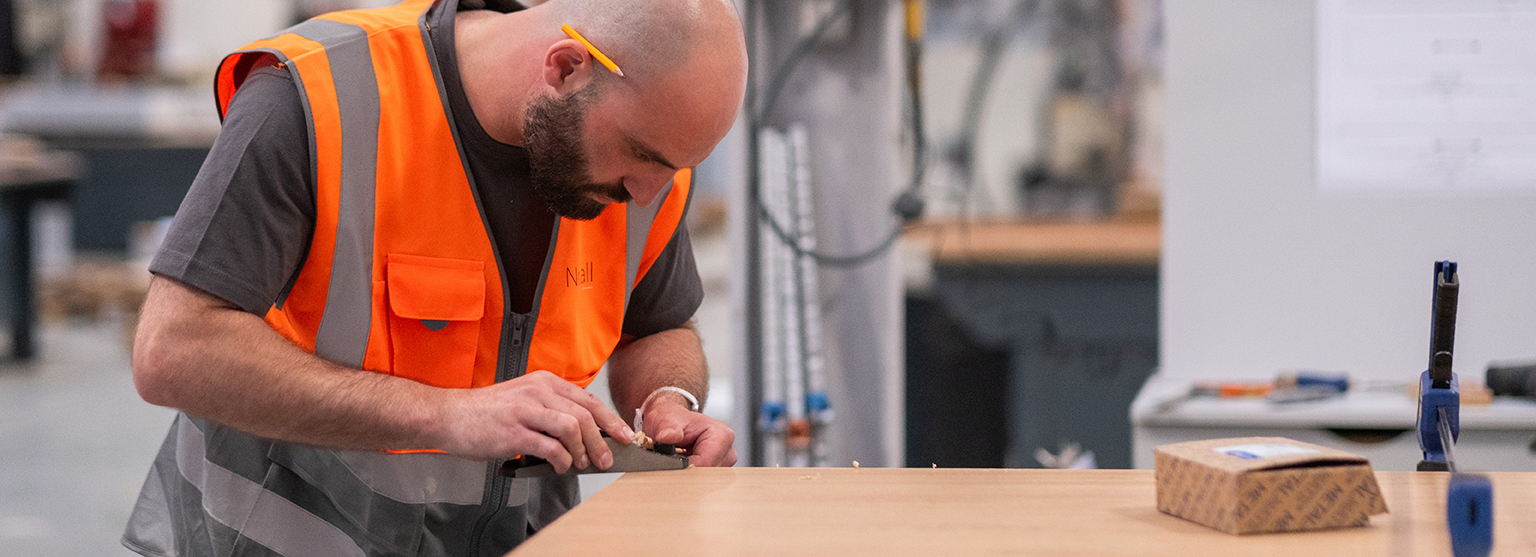 Skilled craftsman sanding and finishing wood in Nuttall’s UK manufacturing facility, representing craftsmanship and precision in British retail design.